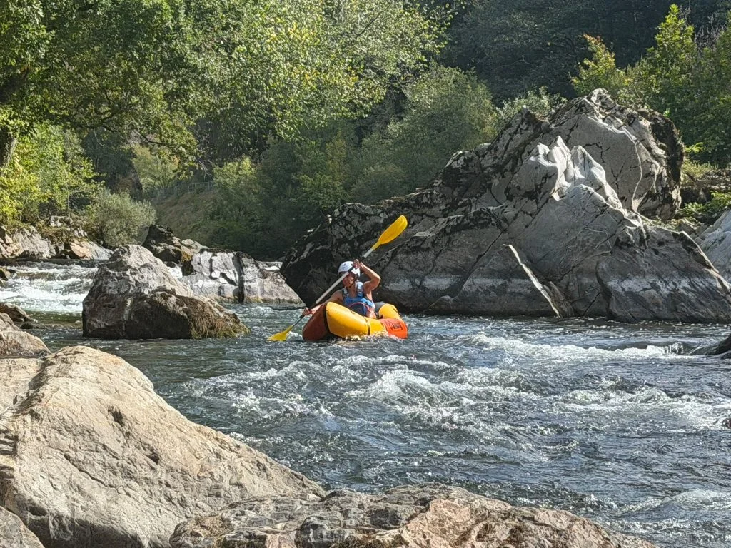 Une participante équipée d'un casque blanc pagaie entre les rochers dans un passage d'eau vive sur la Nive.